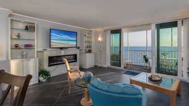 Un salon moderne doté d’un téléviseur à écran plat, d’une cheminée et d’un balcon offrant une vue sur la mer.