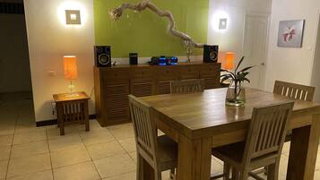 Un coin repas avec une table et des chaises en bois, une lampe, un haut-parleur et un mur vert agrémenté d’une décoration en forme de branche.