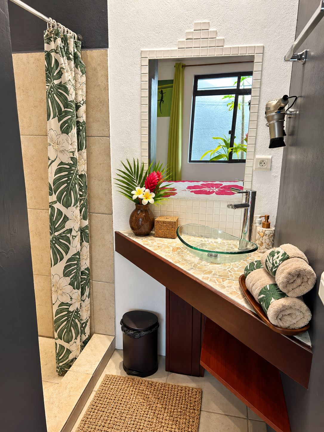 A bathroom with a shower curtain, a glass sink, a mirror, a window with a view, and towels on the counter.