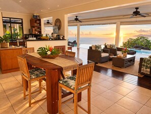 A spacious living area with a wooden dining table, comfortable seating, and a view of the ocean.