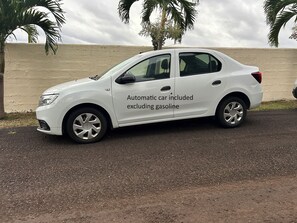 Een witte auto geparkeerd op een zandweg, met palmbomen op de achtergrond.