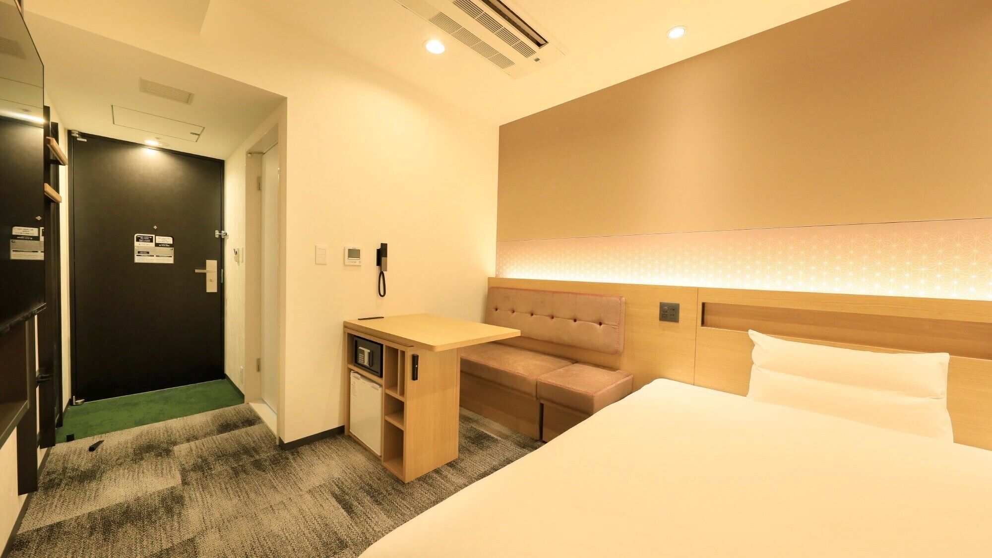 A hotel room with a bed, a desk, a chair, and a small seating area.