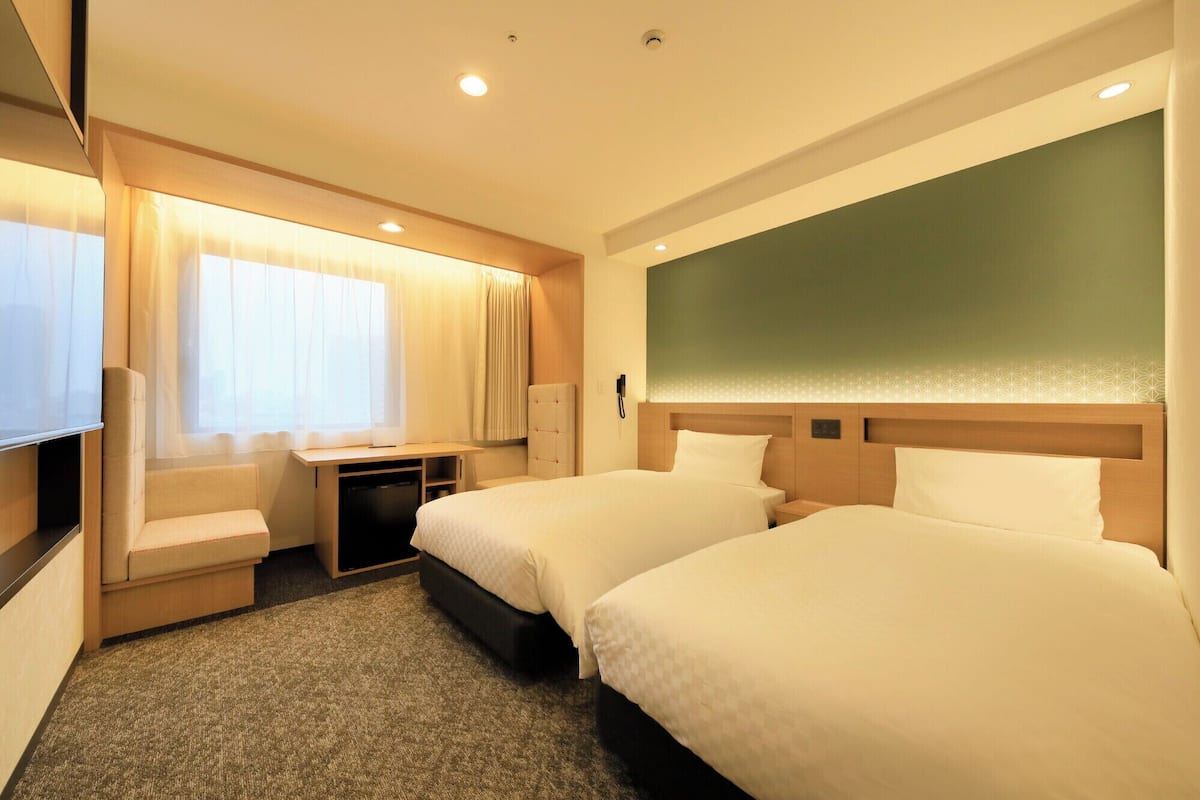 Une chambre d’hôtel avec deux lits, un bureau, une chaise, une télévision et un téléphone.