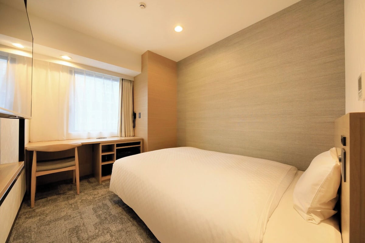 Une chambre d’hôtel avec un lit, un bureau, une chaise et une fenêtre avec des rideaux.