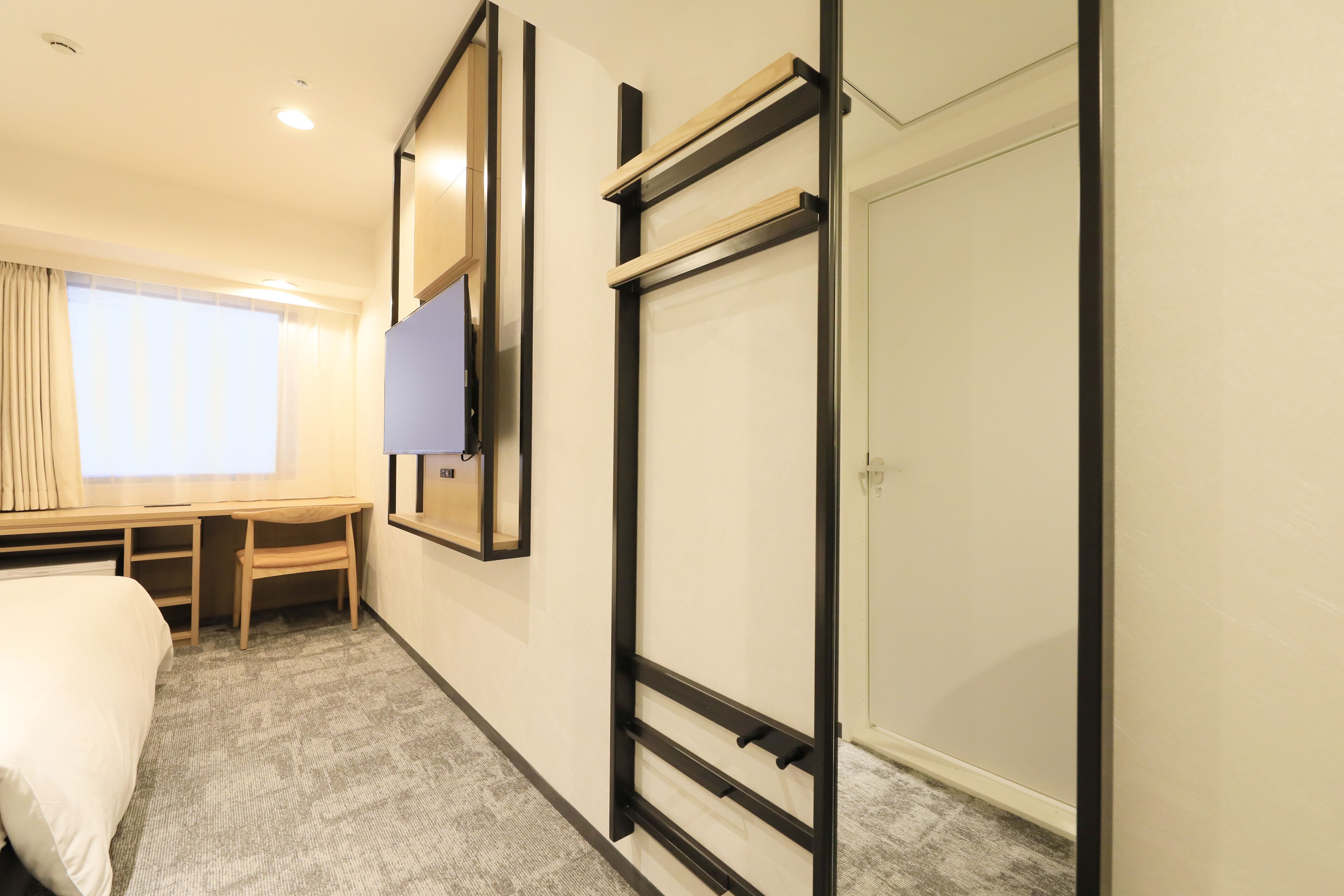 A hotel room with a bed, a desk, a TV, and a wardrobe.