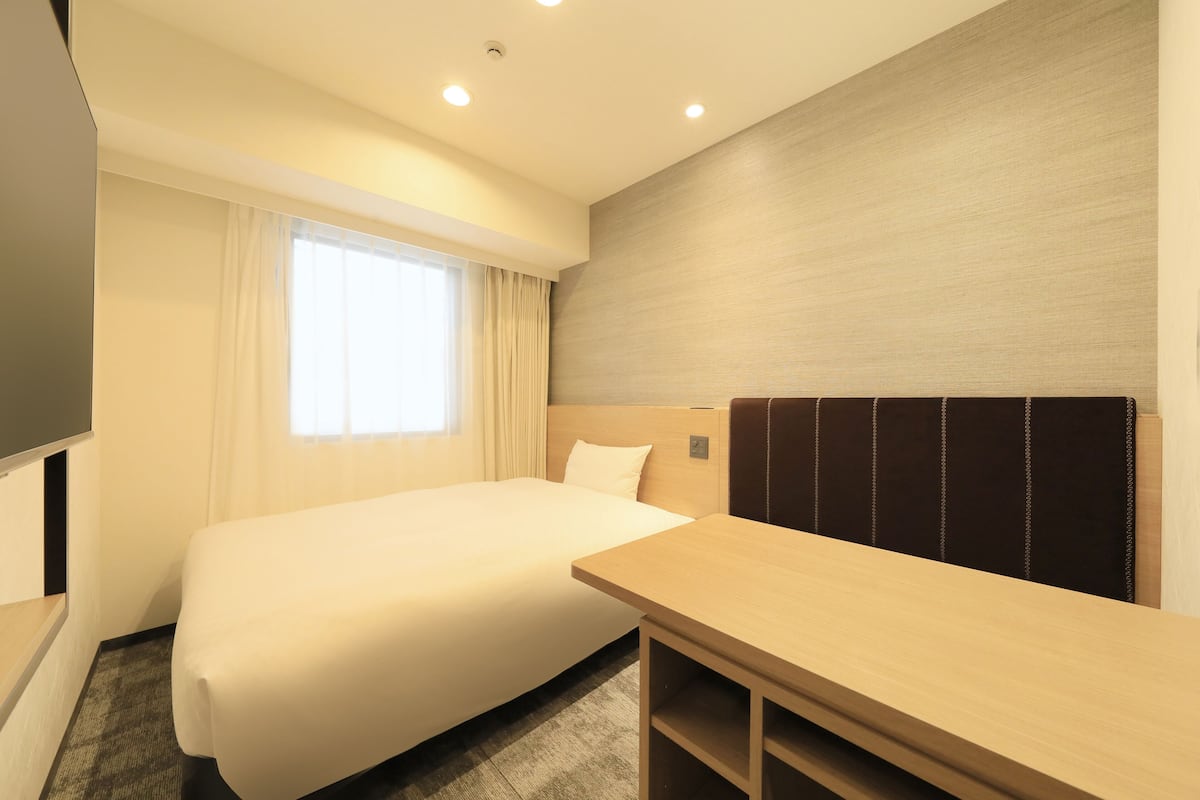 Une chambre d’hôtel avec un grand lit, un bureau en bois, un téléviseur à écran plat et une fenêtre avec des rideaux.