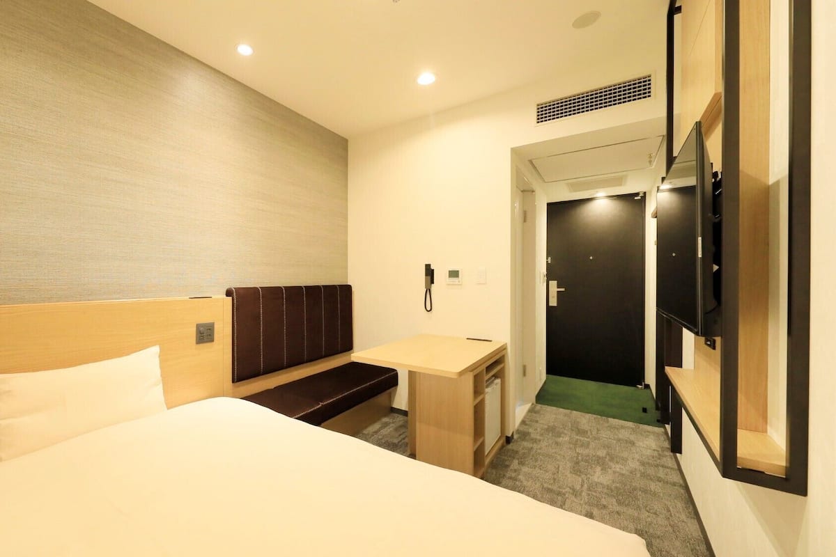 Une chambre d’hôtel avec un lit, un bureau, une banquette, une télévision et une porte.