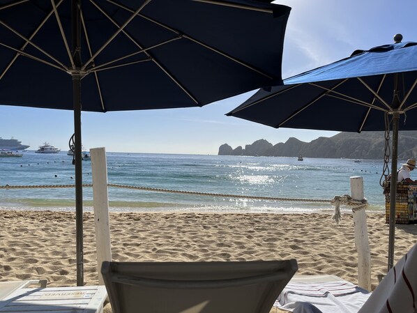 A beach with umbrellas, a chair, and a view of the sea and boats.