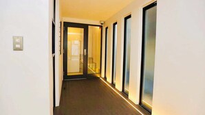 A hallway with a carpeted floor, a door with a glass panel, and a light fixture on the ceiling. - TIME SHARING STAY ikebukuro (Tokyo)