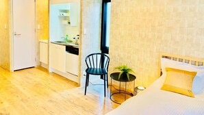 A hotel room with a bed, a small table with a plant, a chair, a kitchenette, and a door. - TIME SHARING STAY ikebukuro (Tokyo)