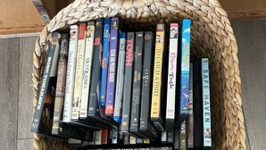 Una cistella teixida plena de DVD i llibres damunt un terra de fusta.