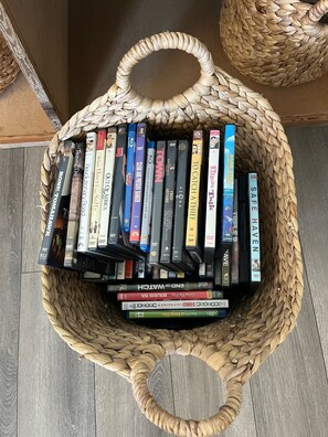 A woven basket filled with DVDs and books on a wooden floor. - Original Beach front Cottage (Holden Beach)