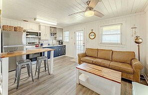 A kitchen with a central island, bar stools, a brown leather sofa, and a ceiling fan. - Original Beach front Cottage (Holden Beach)