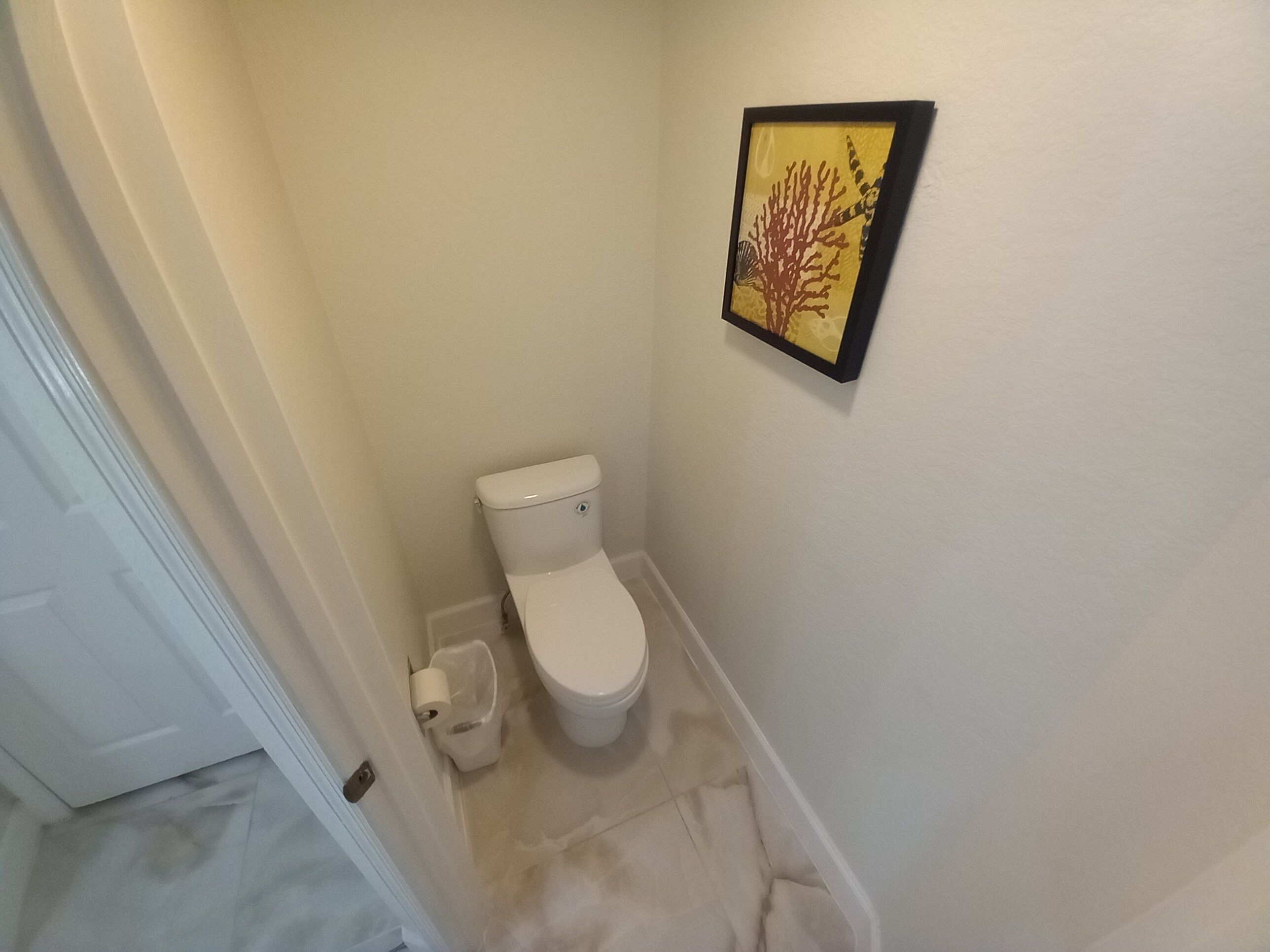 A small, clean bathroom with a toilet, a trash can, and a framed picture on the wall.