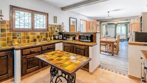 Una cocina con salpicadero de azulejos, armarios de madera, una isla central y una zona de comedor con mesa y sillas.