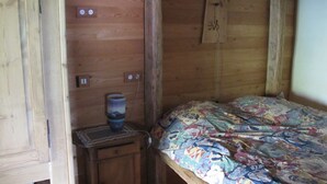A wooden cabin room with a bed, a small table, and a wall-mounted shelf. - Farmhouse in a mountain village hamlet (La Roche-de-Rame)