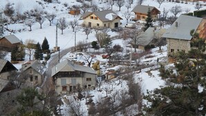 A snow-covered residential area with houses, some with visible chimneys and windows, and a few trees. - Farmhouse in a mountain village hamlet (La Roche-de-Rame)