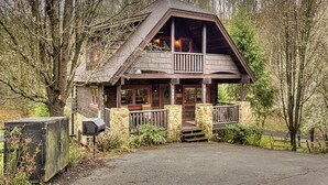 A rustic cabin with a stone foundation, a wooden deck, and a porch with a railing. - Hillside Dreams #265 (Sevierville)