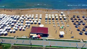 An aerial view of a beach with rows of umbrellas and sun loungers, a building with a red roof, and the ocean in the background. - Akalia Resort Hotel (Manavgat)