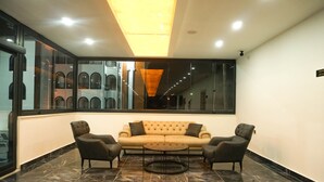 A modern lounge area with a sofa and armchairs, a round coffee table, and a large window offering a view of a building with arched windows. - Akalia Resort Hotel (Manavgat)