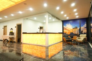 A hotel reception area with a marble floor, a reception desk, and a mural of a sunset. - Akalia Resort Hotel (Manavgat)