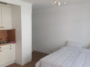 A bedroom with a bed, a white wardrobe, a kitchen area with a sink, and a ceiling light fixture. - Studio rue d'antibes (Cannes)
