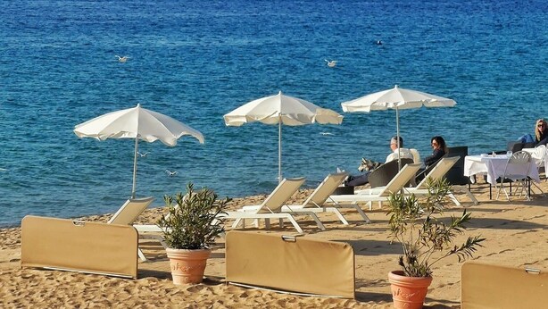 A beach with lounge chairs and umbrellas, a clear view of the sea, and mountains in the background.
