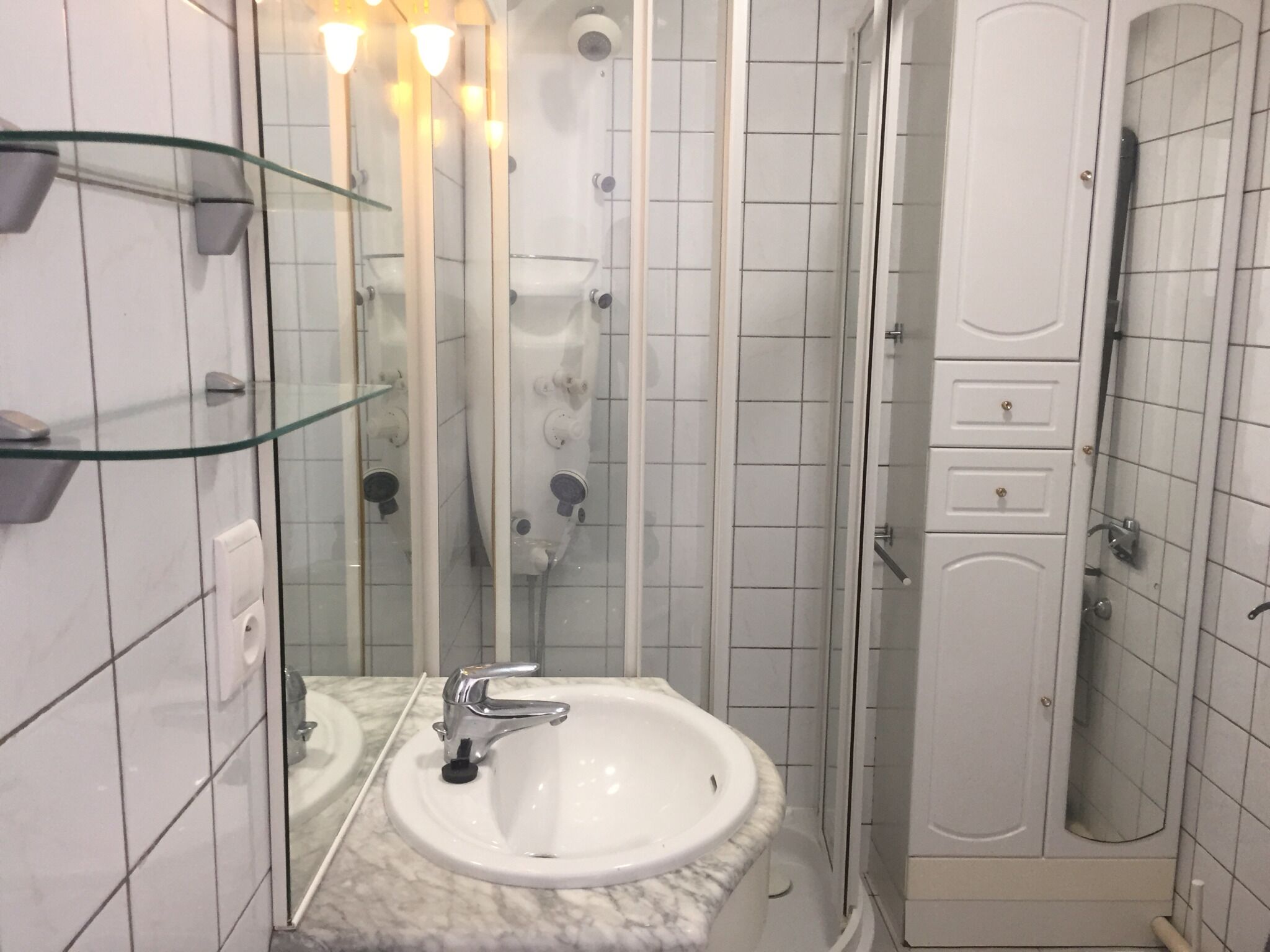 A bathroom with a white sink, glass shower enclosure, and a white door.