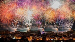 A nighttime cityscape with multiple fireworks displays over a body of water.