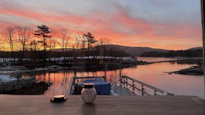 Vista de un río al atardecer con un muelle y una mesa con un florero y una vela.