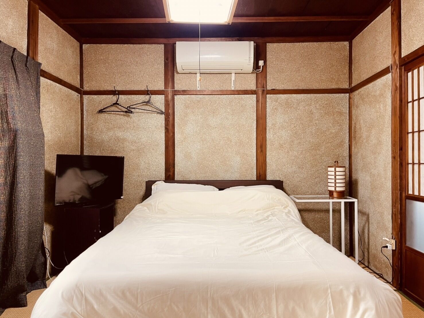 Un dormitorio con cama, televisión, aire acondicionado y una mesita de noche con lámpara.