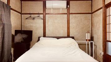 Un dormitorio con cama, televisión, aire acondicionado y una mesita de noche con lámpara.