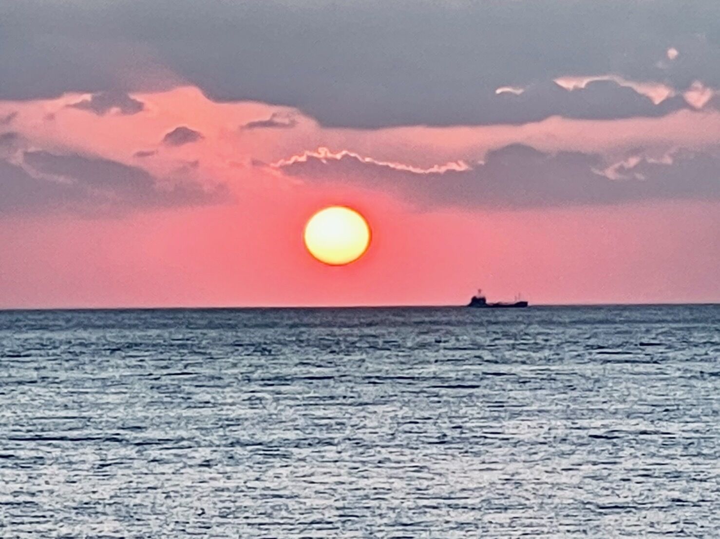 A sunset over the ocean with a ship in the distance.
