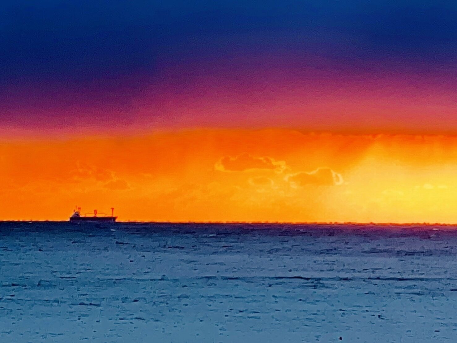 Un coucher de soleil sur une mer calme, avec un navire à l'horizon.