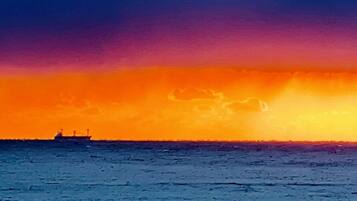 Un coucher de soleil sur une mer calme, avec un navire à l'horizon.