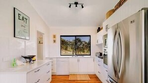 Una cocina moderna con armarios blancos, un refrigerador de acero inoxidable y un ventanal con vistas a palmeras.