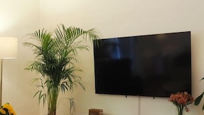 Olohuoneessa on taulutelevisio, ruukussa oleva viherkasvi, pieni pöytä maljakolla ja valkoinen mediakeskus.