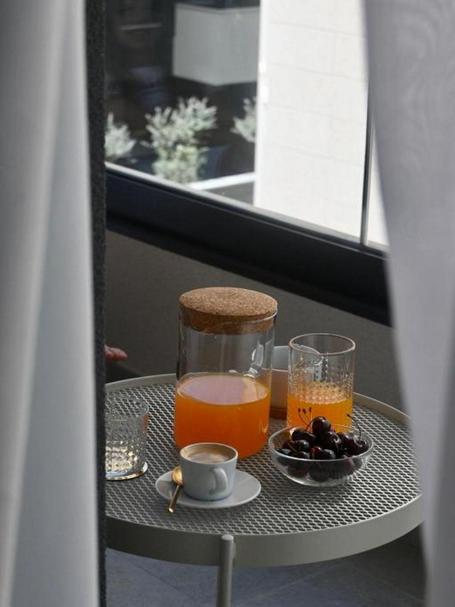 A table with a drink, a cup, and a bowl of cherries.