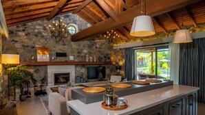 A spacious living area with a stone fireplace, a large island with a coffee pot, and a view of the outdoors. - Kaya Villas Exclusive (Fethiye)