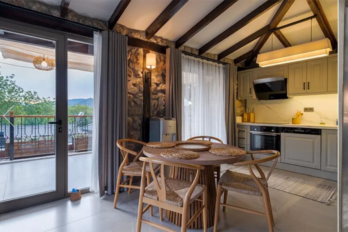 A modern kitchen with a dining area, a stone wall, and a bathroom with a large mirror and sink.