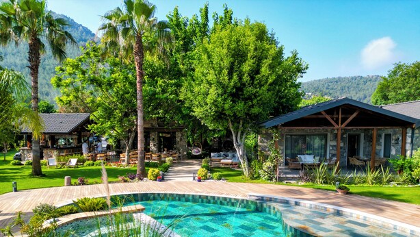 A resort with a swimming pool, outdoor seating, and a stone building. - Kaya Villas Exclusive (Fethiye)