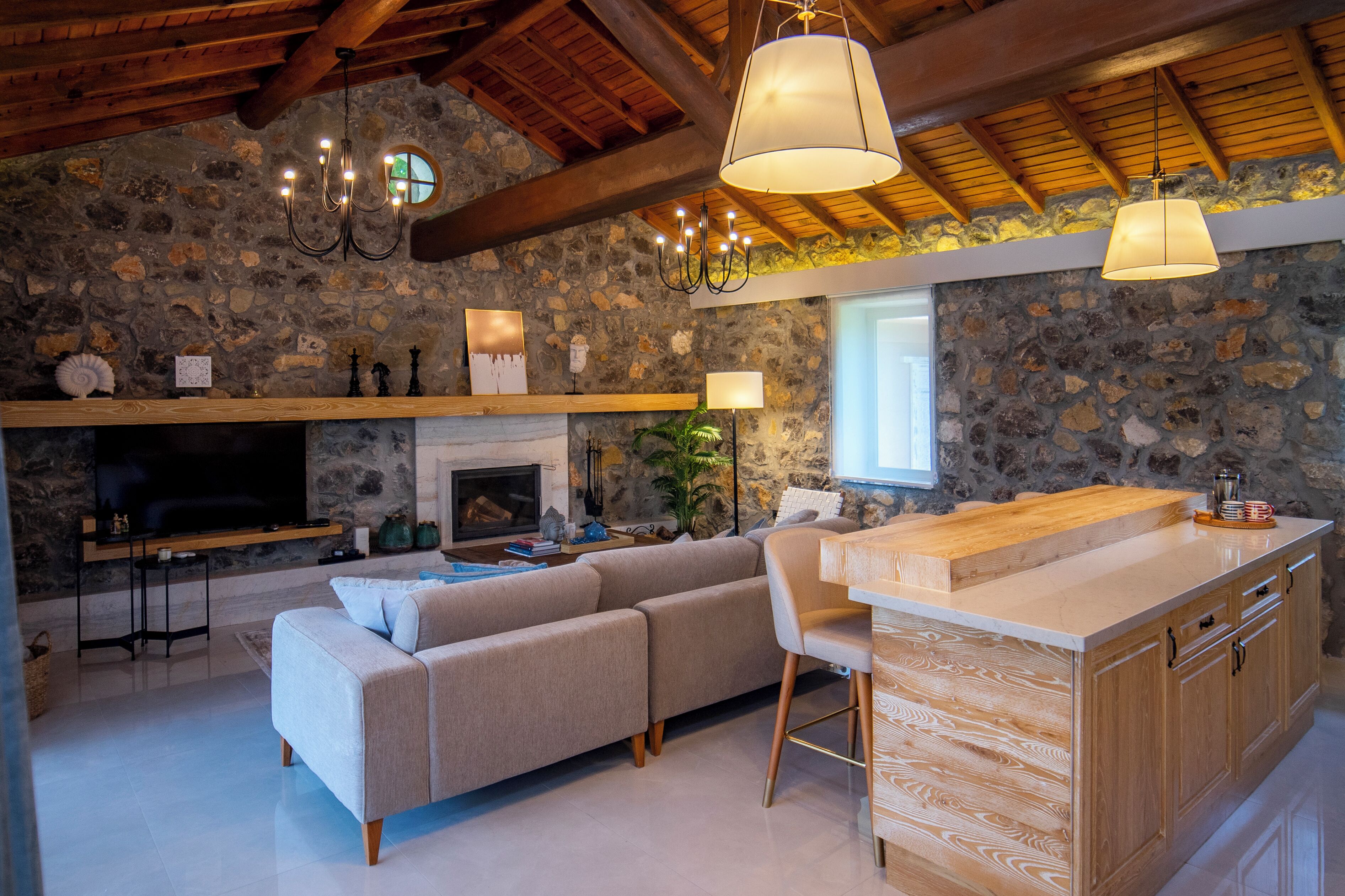 A cozy living room with a stone wall, a fireplace, a sofa, and a wooden dining area.