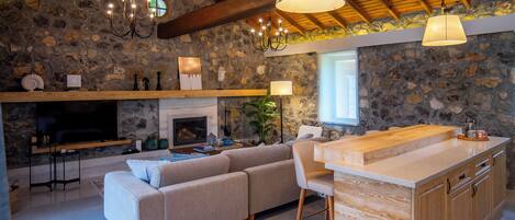 A cozy living room with a stone wall, a fireplace, a sofa, and a wooden dining area.