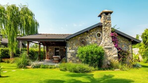 A stone house with a chimney, surrounded by lush greenery and a patio with outdoor furniture. - Kaya Villas Exclusive (Fethiye)