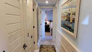 A hallway with white doors, a patterned rug, and a painting of a coastal scene. - CP 614 Golf Course View Condo - Paradise Vacation Rental in Ocean Village (Fort Pierce)