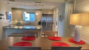 A modern kitchen with a central island, wooden chairs, and a dining table with red placemats. - CP 614 Golf Course View Condo - Paradise Vacation Rental in Ocean Village (Fort Pierce)