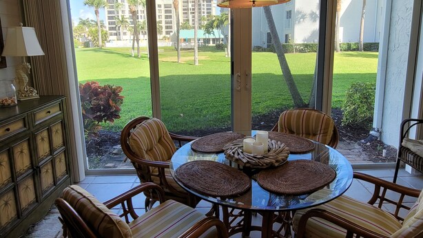 A dining area with a round glass table, wicker placemats, and striped cushioned chairs. - CP 614 Golf Course View Condo - Paradise Vacation Rental in Ocean Village (Fort Pierce)