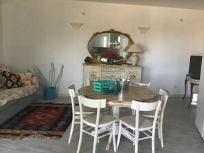 A dining area with a round table, white chairs, and a decorative mirror above.