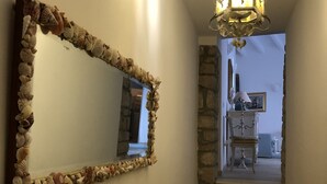 Un couloir orné d’un miroir encadré de coquillages, d’un escalier et d’un lustre.