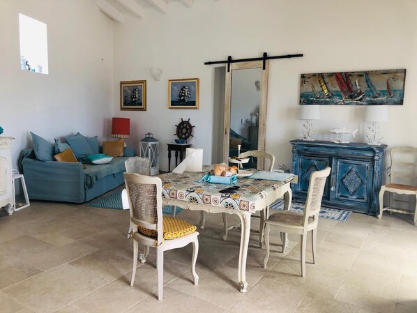 A dining area with a table set for two, a blue sofa, a mirror, and a painting on the wall.